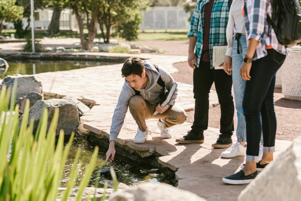 pexels-photo-7683683-7683683 Group of college students interacting with pond nature during study session outdoors.
